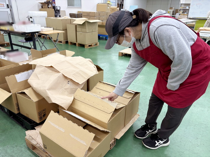 段ボールを前に入荷を取る女性スタッフ
