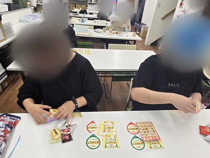 『じゃがりこメーカー』で作成したラベルを紙コップに丁寧に貼り付け、パッケージを自作する指先の訓練