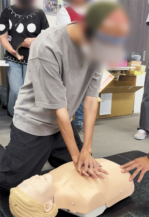 消防士のアドバイスを受けながら、見ている以上に体力と正確さが求められる胸骨圧迫に、全身を使って一生懸命に取り組む訓練生。