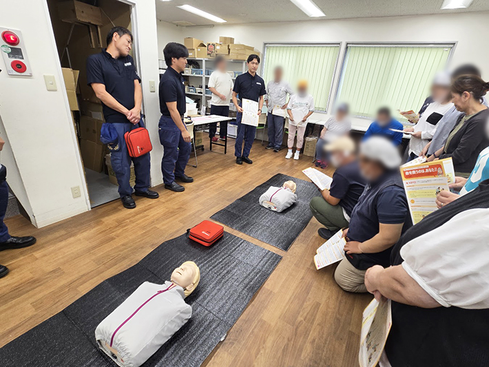 弥富市のオリーブ（就労継続支援B型）にて、海部南部消防署の職員を講師に招き、室内で心肺蘇生法の基礎知識を学ぶ訓練生とスタッフの様子。