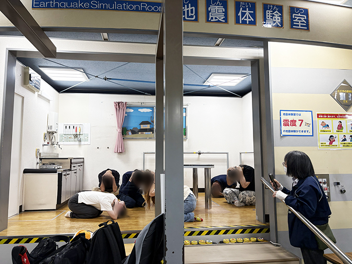 地震発生時の基本動作として、座った状態で頭を低く下げ、落下物から身を守るための姿勢を必死に保とうとする訓練生。