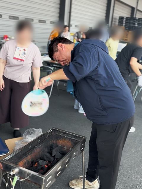 1階の軒下スペースにて、渡邉理事長が炭への着火方法や安全な火の扱い方を実演して教えている場面。