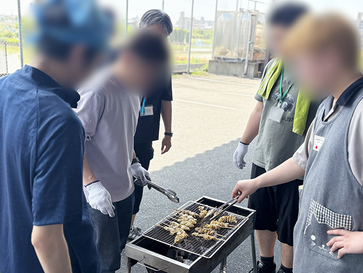 BBQ網の上で、タレの香ばしい匂いが立ち上る焼き鳥を一本ずつ丁寧に裏返して焼いている様子。