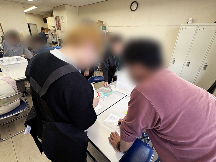 朝礼後、食堂に集まった参加者が、洗う、剥く、切るなどの調理担当を話し合って決めている様子。