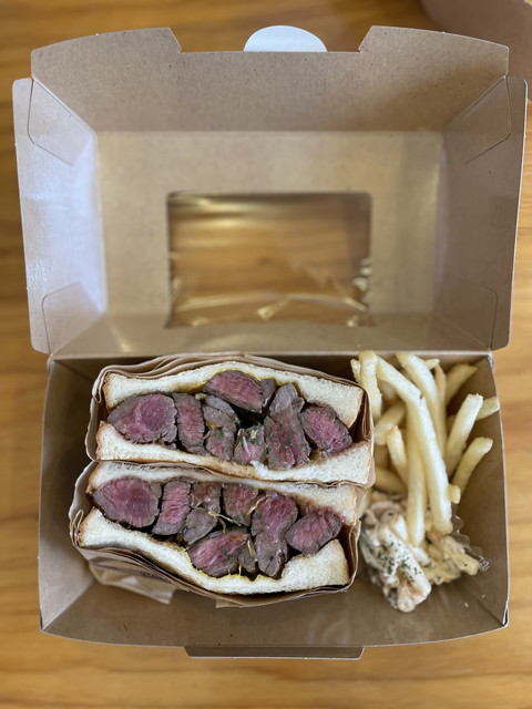 看板メニューの「ステーキサンド20feet」。厚切りで肉肉しいステーキがサンドされ、揚げたてのフライドポテトが添えられた、ボリューム満点の一皿。