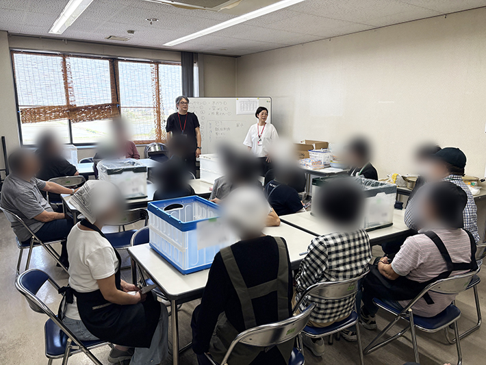 ホワイトボードを使い、スタッフがカレー調理の手順や包丁、火の取り扱いに関する安全管理を説明する風景。