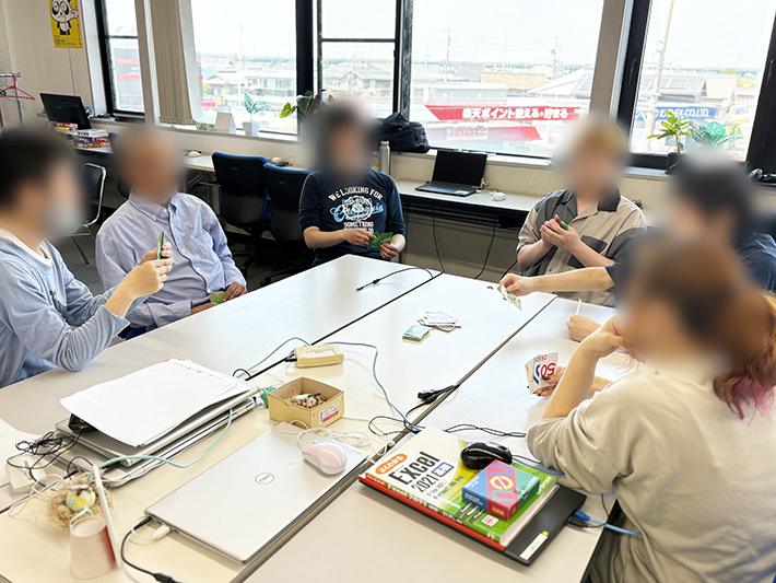 冷房の効いたITルームで、カードゲーム「neu(ノイ)」を通じて利用者同士のリフレッシュと交流を楽しむ風景。