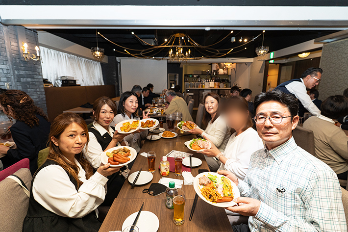 フレーベルのスタッフが懇親会の料理を手に、和気あいあいとした雰囲気で撮影を楽しむ様子。事業所の団結力が伝わる一枚