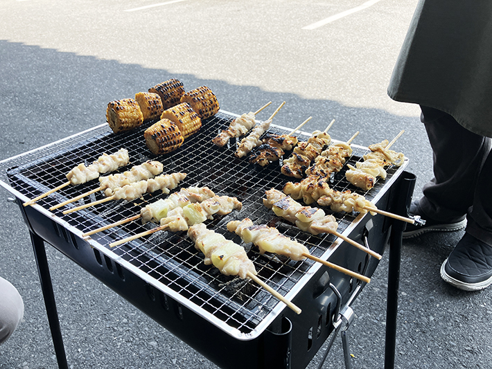 網の上で並んで焼かれている、ジューシーな焼き鳥と甘い醤油の香りが漂う焼きトウモロコシ。