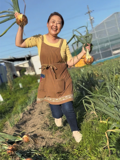 両手いっぱいに収穫した玉ねぎを持ち、満面の笑顔を見せるフレーベルスタッフ。日々の努力が形になった最高の瞬間