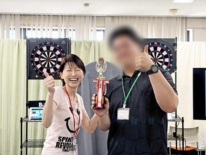 激戦を制し、見事3年ぶりに訓練生として優勝を飾ったチャンピオンの姿。スタッフから祝福を受け、輝くトロフィーを手に自信に満ちたサムズアップで喜びを表現する瞬間。