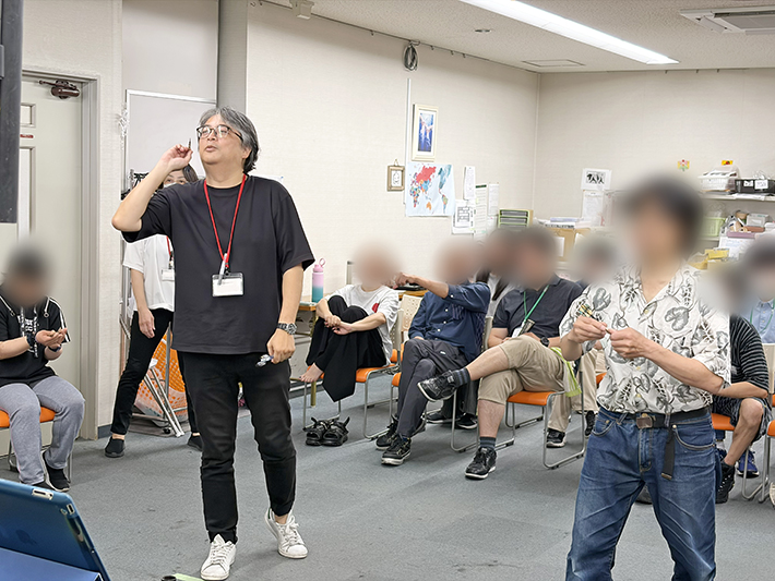 「スタッフには負けないぞ」と意気込む訓練生たちの挑戦を受け、自らもダーツを投じるスタッフ。利用者と支援員が同じ目線で楽しみ、信頼関係を深めるコミュニケーションの場面。