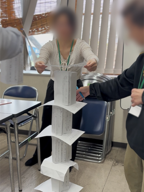 A4用紙20枚という限られた資材を使い、ハサミやテープを使わずに、チームで協力して慎重に紙を積み上げて高さを競う訓練生たち。