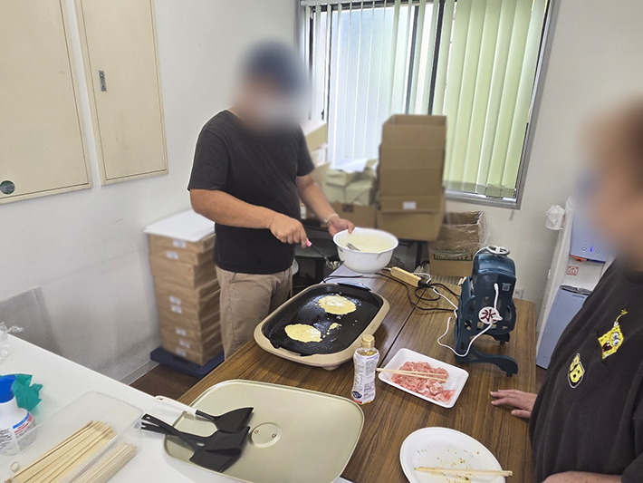 訓練生がお好み焼きの生地を丁寧にホットプレートへ流し込む様子。グループで協力しながら、バランス良く焼き上がるよう真剣な表情で取り組むレクリエーション中のひとコマ。