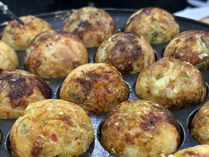 弥富市のフレーベルで開催された「たこ焼き風パーチー」にて、たこ焼き器でこんがりと焼き上がるたこ焼き。これまでで最高の参加人数となり、会場全体が大賑わいの中で調理が進む様子。