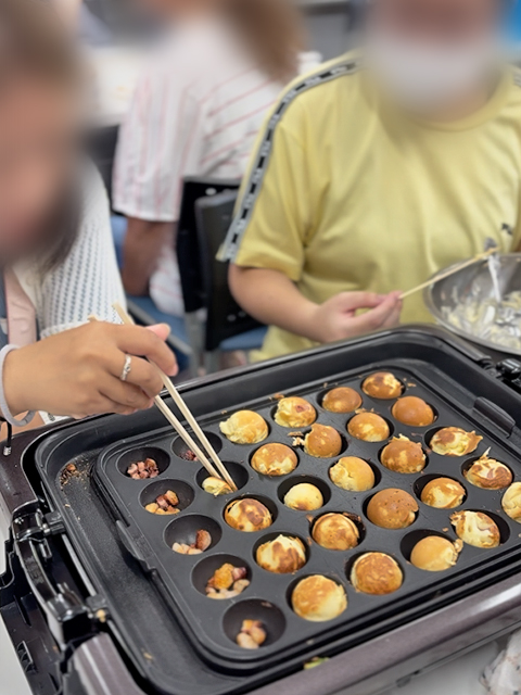 たこパの締めくくりとして、たこ焼き器を活用してベビーカステラを焼く様子。訓練生自ら粉や牛乳を計量して生地を作り、余ったウィンナーを入れてアメリカンドッグ風にアレンジするなど、自由な発想でデザート作りを楽しむフレーベルの訓練風景。