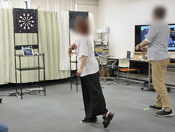 集中力を高め、ダーツボードの得点エリアを鋭い眼差しで狙う訓練生。ポイント制の個人戦において、一投一投に全力を尽くす真剣な表情が印象的な場面。