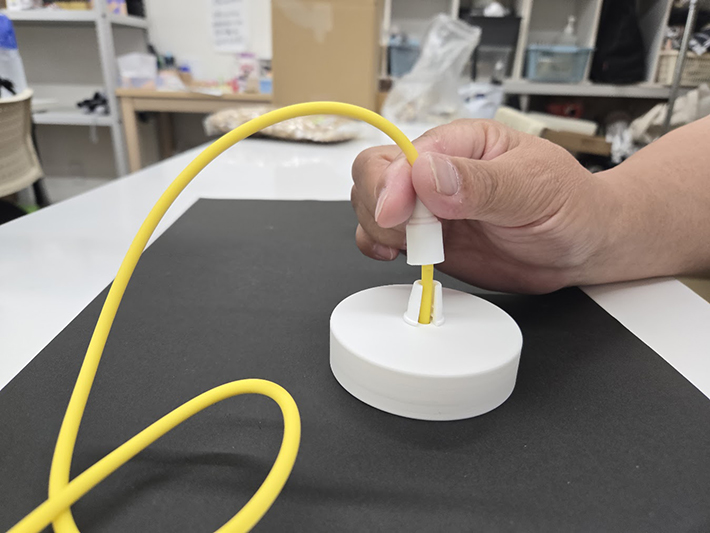 通した紐の端を治具の固定スリットにセットする様子。指先だけで紐を支える必要がなくなり、握力の弱い利用者でも次の部品取り付けに向けて確実かつ安全に準備ができる。