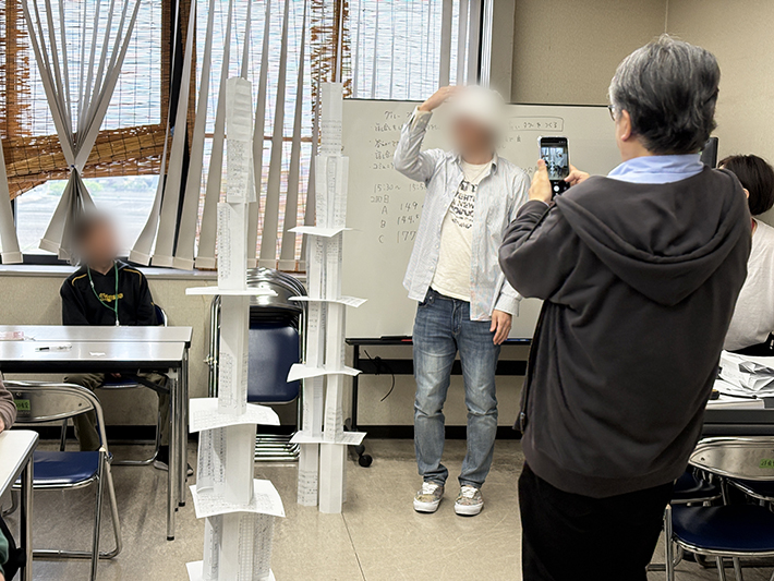 自分たちの身長を超えるほどの高さまで積み上がったタワーに驚き、工夫次第で大きな目標を達成できるという「自信」に満ちた笑顔の瞬間。