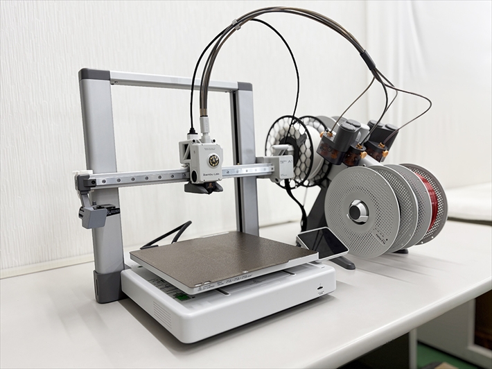 障碍者ITカレッジ愛西に導入された3Dプリンター。利用者が「部品の取り付けで指が痛くなる」という課題を解決するため、作業を補助する専用器具『治具（じぐ）』を自社で設計・造形している様子。