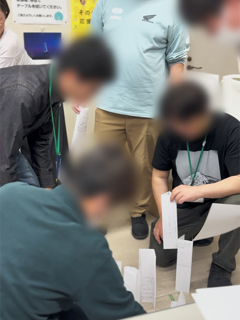 タワーの重さを支えるために、最も重要となる「土台」の形を工夫し、一本ずつ丁寧に紙を配置していく基礎工程の作業風景。