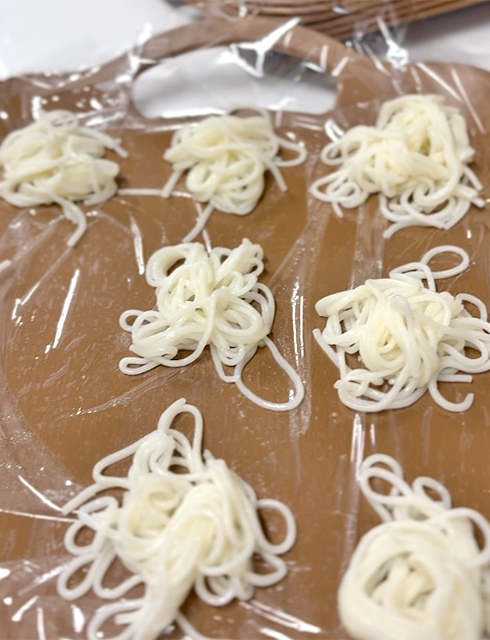 フレーベルの「わんこ素麺」レクリエーションに向けて、まな板の上に一口サイズに小分けして並べられた茹でたての素麺。フレーベル農園で収穫されたばかりの新鮮な葱(ねぎ)と紫蘇(しそ)の薬味も用意され、賑やかな大食いチャレンジの準備が整った様子。