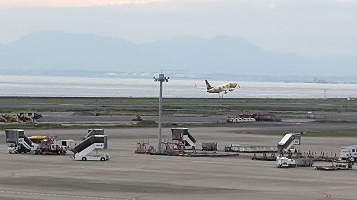 中部国際空港セントレアのスカイデッキから遠くに望む、離陸の瞬間を迎えたスカイマークの特別塗装機「ピカチュウジェット」。青空へ向かって力強く上昇を始める、旅の始まりを感じさせる一枚。