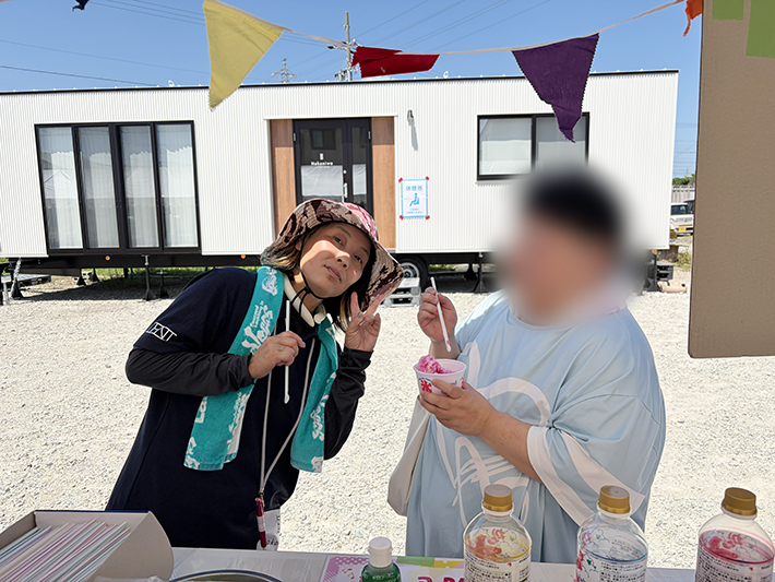 出来立てのかき氷をふるまい、隣の来場者にピースサインを送るフレーベルのスタッフ。美味しい食べ物を囲んで自然と会話が生まれ、地域住民とスタッフの信頼関係が深まる、お祭りならではの交流シーン。