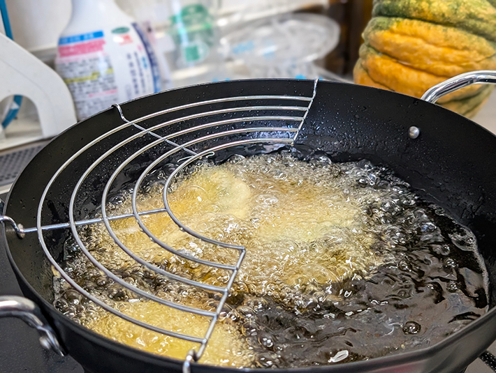 油の中でパチパチと小気味良い音を立てながら、カラッと揚げられているカボチャの天ぷら。採れたてのカボチャのホクホク感と、豊かな甘みを最大限に引き出すために、衣をサクサクに仕上げるこだわりの揚げ物調理の風景。