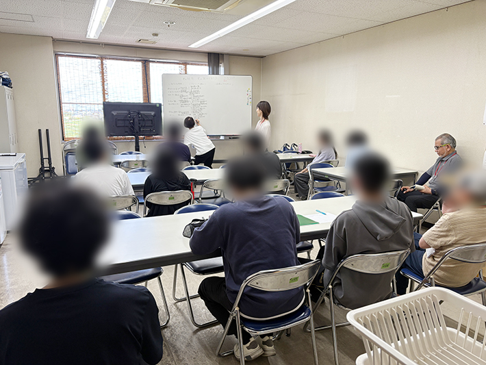 リフレーミングの講義風景:例を書き出すスタッフと、席で聞いている訓練生