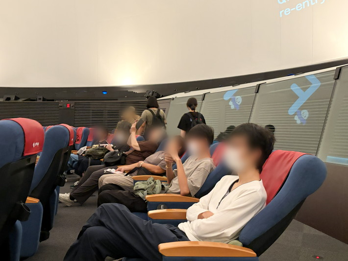 ゆったりとしたリクライニングシートに座り、上映開始を心待ちにする訓練生たち。日頃の訓練を離れ、専門の学芸員によるその日限りの星空解説を通じて、宇宙のロマンと科学の不思議に触れる教養の時間。