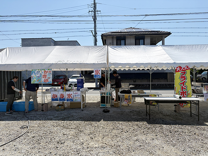 屋外に設置された特設屋台にて、かき氷やフライドポテトの準備に励むスタッフたち。厳しい暑さの中でも、来場者に美味しい「おもてなし」を届けるため、笑顔で準備を進める活気ある一コマ。