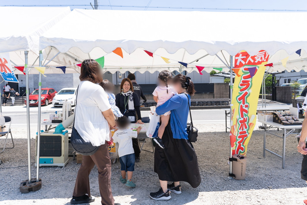 真夏の日差しのなか、賑わうフレーベルイベント会場 (屋台でお客さんと談笑するスタッフ)