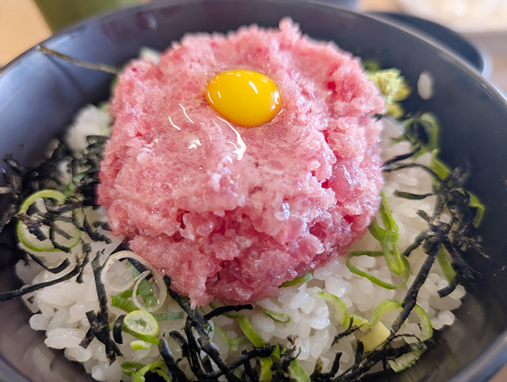 ねぎとろ丼（まぐろたたき丼）のクローズアップ写真。酢飯の上に刻み海苔と刻みネギが敷かれ、その上にこんもりと盛られた新鮮なまぐろのたたきと、中央に飾られた黄色く輝く卵黄が食欲をそそる、まぐろレストラン自慢の人気メニュー。