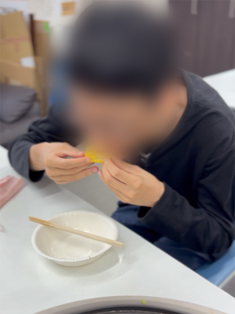 香ばしくジューシーに焼き上がった出来立てのトウモロコシを両手で持ち、美味しそうに大きくかぶりつく訓練生。自分たちの手で育ててきたからこそ、最高の甘みと格別の美味しさに満面の笑みがこぼれる瞬間。