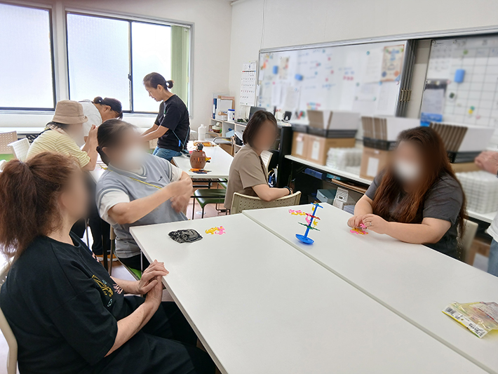 ヤシの木のタワーからお猿のコマを落とさないようにスティックを抜き取るアクションゲーム「お猿のゲーム」を楽しむテーブル風景。ハラハラドキドキのルールに歓声が上がり、順番を待つ時間も会話が弾むレクリエーションの様子。