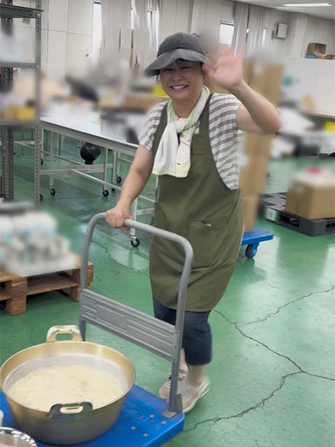 調理室で作られた大量の特製つけダレが入った大きな鍋を、台車に乗せて慎重に流しそうめん会場へと運ぶスタッフの様子。大人数の訓練生やスタッフに出来立ての美味しさを届けるための、ナベ'sキッチンならではの本格的な炊き出しの一幕。