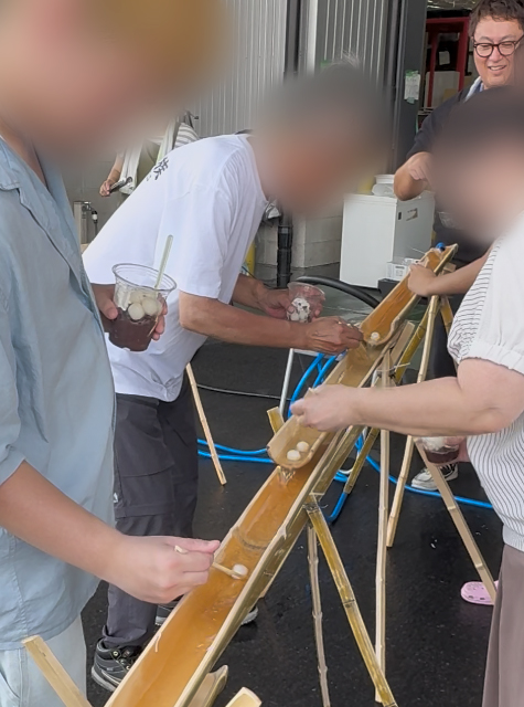竹の流しそうめん台を転がるように流れてくる、まん丸でモチモチとした白玉をタイミングよくキャッチしようとする訓練生たち。掴みにくい丸い食材に苦戦しながらも、お互いにコツを教え合い、歓声を上げて楽しんでいる賑やかな一幕。