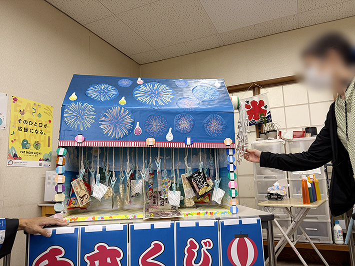 まきの木の訓練生（利用者様）が手作りした華やかなデコレーションで彩られた、お祭りムード満点の千本くじ。どの紐が豪華な景品に繋がっているか分からないドキドキ感を醸し出す。