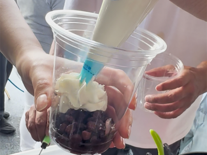 ぜんざい(あんこ)に、豊かなコクをプラスする生クリームをトッピングして、特製クリームぜんざいへと仕上げていく調理工程。和洋折衷のおいしさを追求する、渡邉理事長の「ナベ'sキッチン」らしい細かなこだわり。