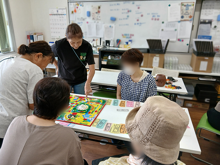 料理の焼き上がりや順番を待つ時間、テーブルを囲んでボードゲーム「人生ゲーム」に夢中になる参加者たち。ルーレットを回してお札やコマを動かしながら、スタッフや仲間と笑顔で交流を深める和気あいあいとしたひととき。