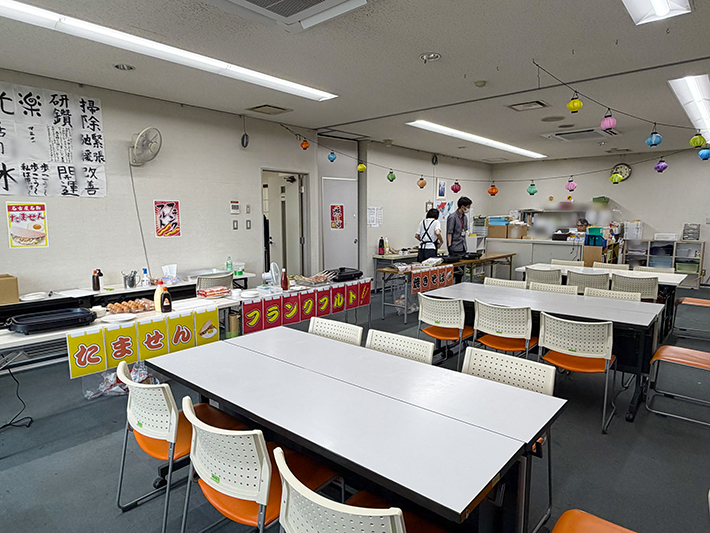 まきの木の訓練室をイベント仕様の屋台街に見立て、たません、フランクフルト、焼きそばの調理ブースを横一列に並べた特設コーナー。香ばしいソースや醤油の香りが立ち込め、室内を歩くだけで本物の縁日に来たような高揚感に満ちた風景。