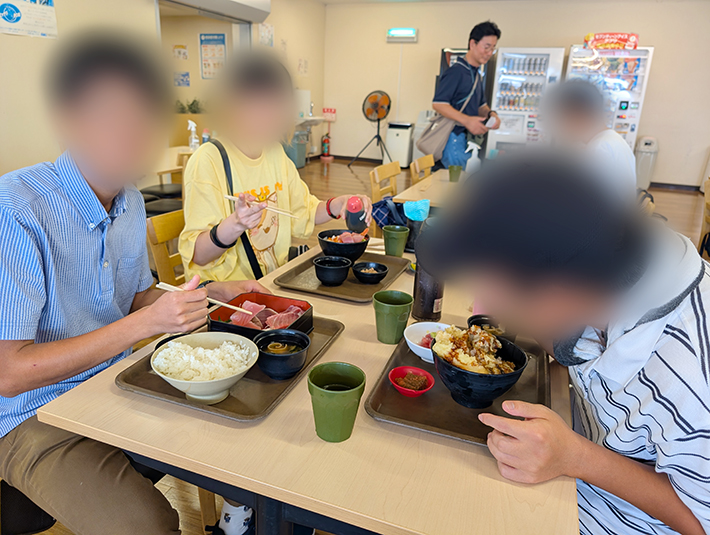 重箱に盛られたまぐろ刺身定食や天丼など、各自が選んだ好みのメニューを美味しそうに味わう訓練生たち。お醤油を回しかけたり、大きな口で頬張ったりしながら、四日市へのドライブと美味しい海鮮を心ゆくまで満喫した大満足のお出かけレクリエーション。