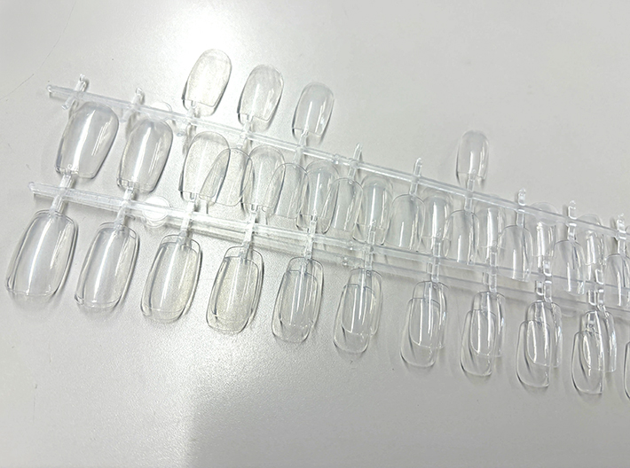プラスチック台紙にサイズ別でずらりと並べられた透明なネイルチップ（つけ爪パーツ）の準備写真。
