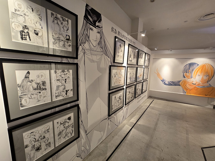 「佐為 塔矢がおまえを見つけた」の銘文壁面と、巨大な佐為のモノクロイラスト、アキラ&ヒカルのカラー原画壁面。