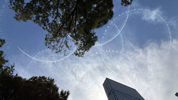 木々の間から見える、ブルーインパルスが空に描いた五輪の煙の輪(一部は木に隠れている)