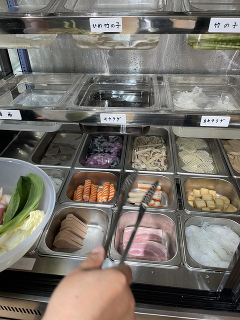 トングを使ってショーケースからキクラゲやひめ竹の子、野菜、お肉などの好みの具材をボウルに取る様子。