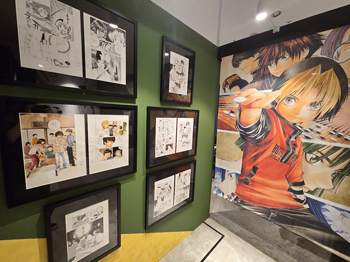 グリーンの壁面に飾られたカラー扉絵や対局原稿と、碁石を構えるヒカルの迫力ある大型イラスト展示。