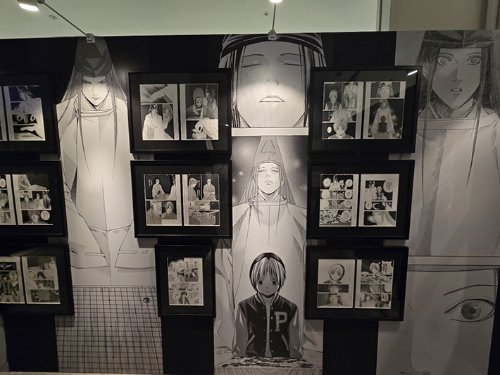 平安衣装の藤原佐為が静かに目を閉じる幻想的な背景壁画と、その周りに飾られた感動的な物語場面の生原稿群。