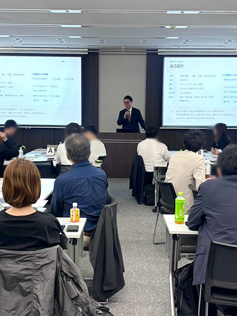 千種地区10月例会の報告に登壇し、自己紹介や過去の失敗談、同友会での学びについてマイクを手に語り始める渡邉盛時理事長。